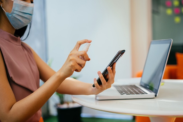 スマートフォンに除菌スプレーを吹きかけている女性